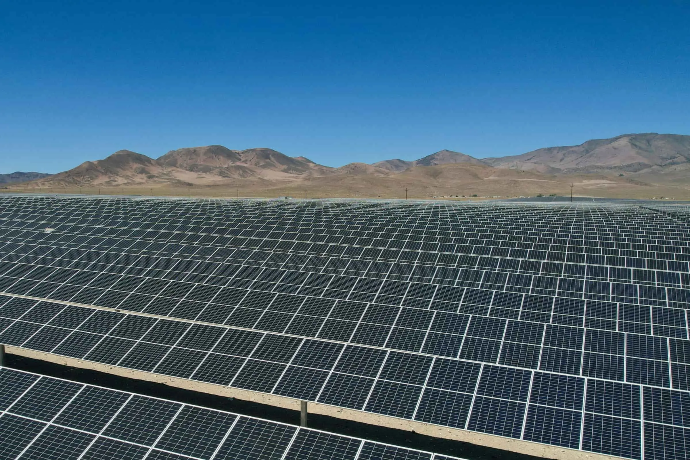 Rows of solar panels on desert ground under a deep blue sky