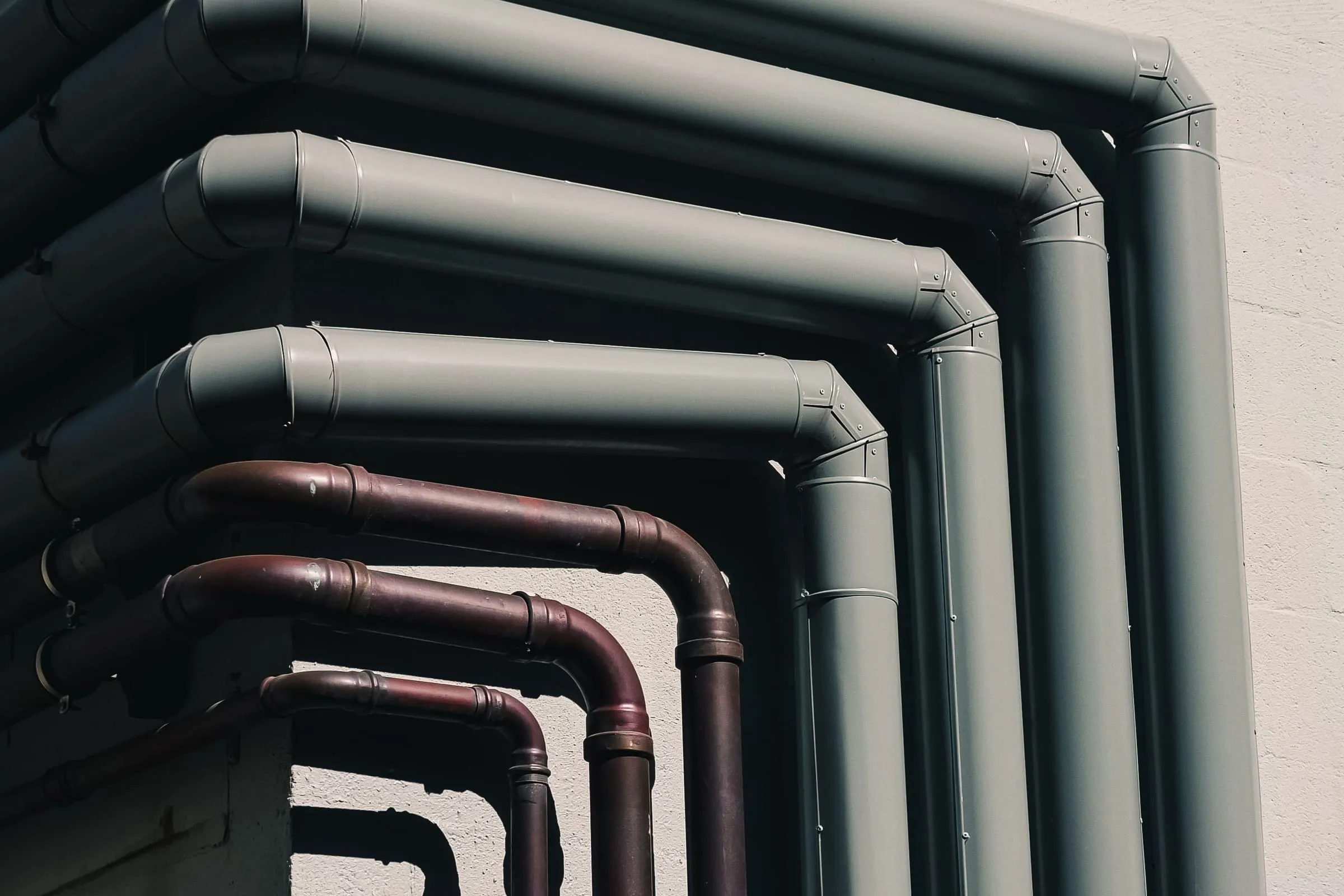 Copper and grey pipework turning a corner on a pale wall